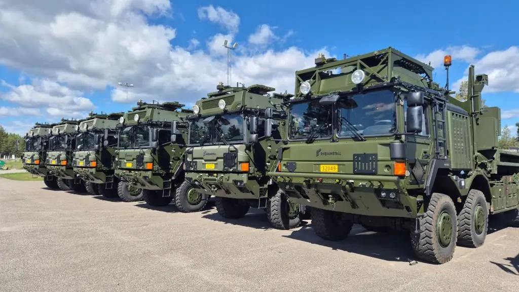 Militära kroklyftlastbilar uppställda utomhus.
